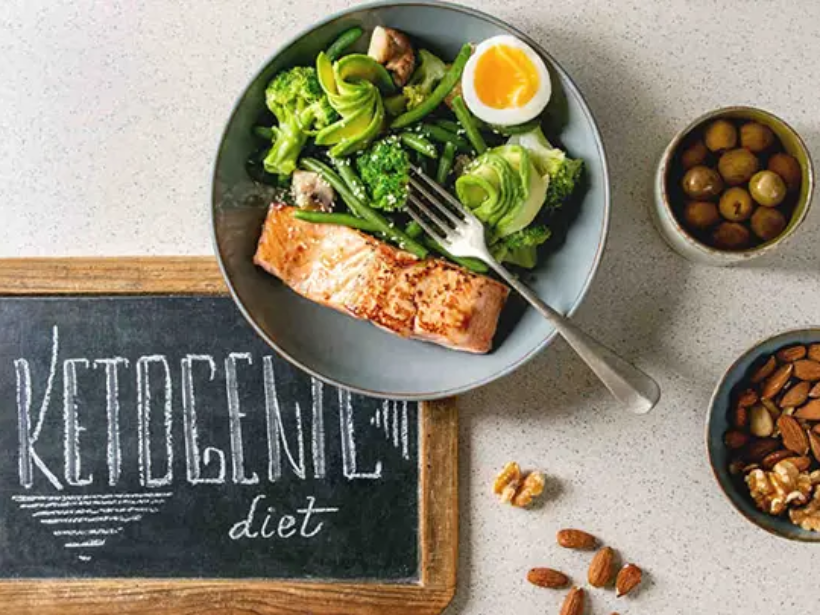 Ketogenic low carb diet dinner grilled salmon, avocado, broccoli, green bean and boiled egg in bowl served with olives, nuts and chalk board lettering over grey spotted background. Flat lay, space