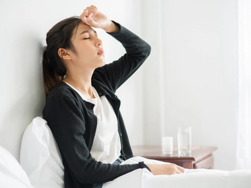An uncomfortable woman sits on the bed and has medicine on the table.